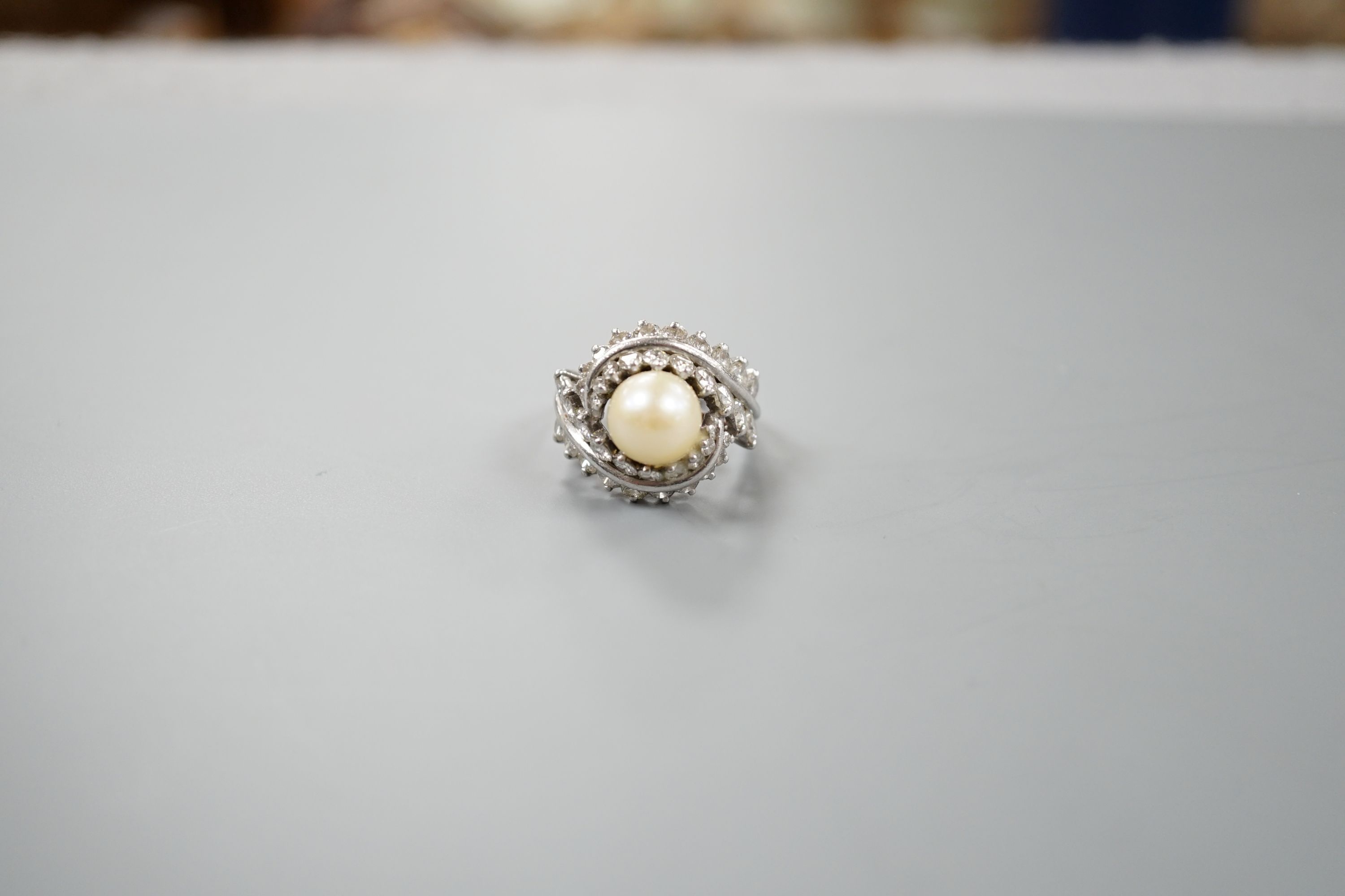 A white metal single stone cultured pearl and diamond cluster set scroll dress ring, size Q, gross weight 13.6 grams.